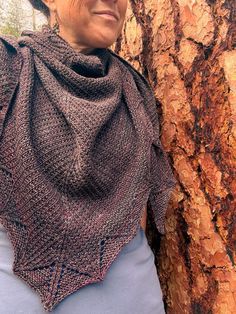 a woman standing next to a tree wearing a knitted shawl over her shoulders