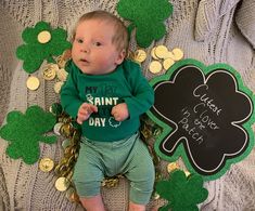 a baby laying on top of a blanket next to shamrocks and gold coins with a st patrick's day sign