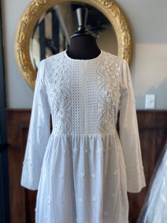 a white dress on a mannequin in front of a mirror and gold framed mirror