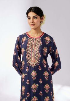 This smart, contemporary collection features a bold floral print, beautifully enhanced with delicate embroidery around the neck. The long-sleeved tunic, crafted from luxurious cotton silk, adds shimmer and richness to the ensemble. Easy to wear and versatile for any occasion, this tunic combines elegance with modern style. Note: Pants are for styling purposes only. Blue Kurta With Embroidered Neckline For Festive Occasions, Festive Blue Kurta With Embroidered Neckline, Designer Embroidered Neckline Kurta Tunic, Designer Embroidered Neckline Tunic Kurta, Eid Floral Print Tunic Kurta, Elegant Blue Floral Print Kurta, Elegant Festive Tunic With Floral Embroidery, Elegant Straight Kurta Tunic With Floral Embroidery, Long Sleeve Cotton Silk Dress With Chikankari Embroidery