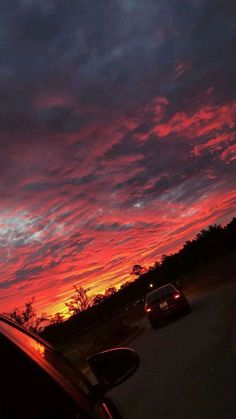 the sun is setting behind some clouds in the sky over a road with cars driving on it