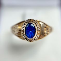 This Vintage 10K Yellow Gold Notre Dame Academy Class Ring features a striking blue oval gemstone at its center, symbolizing school pride and achievement. The gemstone is encircled by the words "Notre Dame Academy," adding a distinguished touch to this classic design. Crafted in 10K yellow gold, the ring showcases intricate detailing on the shank, including school insignias and personalized engravings, reflecting the wearer's connection to their alma mater. With a ring size of 8.25 and a band width of 1.8mm, this ring is both substantial and comfortable, weighing 4.57 grams. This piece is not only a meaningful keepsake but also a timeless piece of jewelry that carries the legacy of a cherished educational institution. School Pride, Alma Mater, Rings Statement, Notre Dame, Timeless Pieces, Class Ring, The Words, Portland, Statement Rings