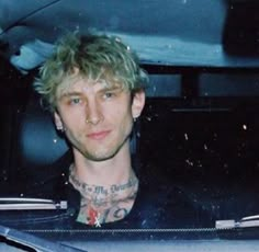 a man sitting in the back seat of a car with tattoos on his chest and neck