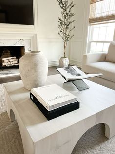 a living room with white furniture and a book on the coffee table in front of a fireplace