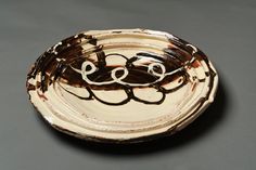 a brown and white plate with two faces drawn on the side, sitting on a gray surface