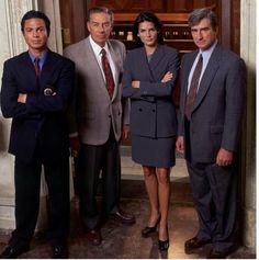 three men and a woman in suits standing next to each other with their arms crossed