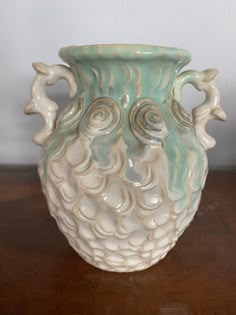 a white and green vase sitting on top of a wooden table next to a wall