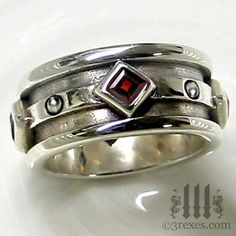 a silver ring with a red stone in the center and two diamonds on each side