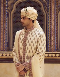 Radiate sophistication in this light beige raw silk sherwani, featuring rich maroon appliqué and zardozi embroidery. Accompanied by a cotton silk choga and churidar, it comes with a striped tissue worked stole. Silk Sherwani With Zari Work For Wedding, Embroidered Art Silk Sherwani For Wedding, Bollywood Style Raw Silk Bandhgala For Traditional Ceremonies, Raw Silk Bandhgala With Dupatta For Traditional Ceremonies, Silk Bandhgala With Naqshi For Wedding, Embroidered Cream Bandhgala For Festivals, Festival Cream Embroidered Bandhgala, Festival Embroidered Cream Bandhgala, Jamawar Sherwani With Intricate Embroidery For Traditional Ceremonies