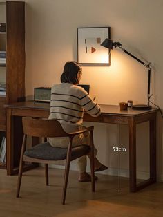 a woman sitting at a desk in front of a lamp with her back turned to the camera