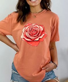 Elevate your wardrobe with this stunning vintage floral shirt featuring a bold, retro-inspired red rose graphic. Perfect for those who love the charm of cottagecore fashion and botanical prints, this flower t-shirt effortlessly combines style and comfort. Whether you're looking for a casual outfit or a unique gift for her, this floral aesthetic shirt is a perfect choice. Made from soft, high-quality fabric, this botanical tee is designed for all-day comfort and durability. The vibrant red rose design adds a pop of color, making it a standout piece in any collection. Whether you're dressing up for a day out in the garden or embracing your inner nature lover, this floral graphic tee is sure to become a favorite. Key Features: Premium Quality: Crafted from breathable, soft fabric that's perfe Spring Rose Print Short Sleeve T-shirt, Summer Rose Print Short Sleeve T-shirt, Summer Short Sleeve T-shirt With Rose Print, Short Sleeve Rose Print Tops For Summer, Pink Rose Print Crew Neck T-shirt, Summer Cotton Tops With Rose Print, Rose Print Tops For Spring, Rose Print Tops For Summer, Spring Cotton T-shirt With Rose Print