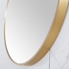 an oval mirror mounted on the wall next to a white marble counter top with gold trim