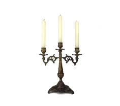 three candles are lit on an ornate metal candelabra against a white background