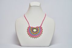 a white mannequin with a pink necklace on it's neck and a green circle bead in the middle