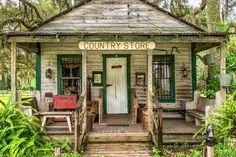 an old country store sits in the middle of some trees and bushes with green doors