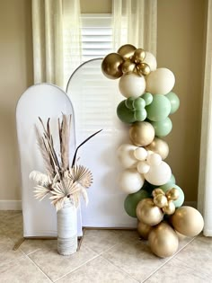 a tall balloon arch with gold, white and green balloons on it next to a vase