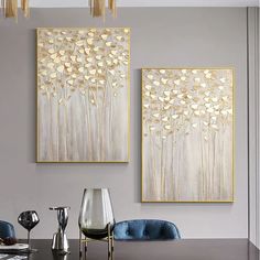 two paintings hanging on the wall above a dining room table with blue chairs and silver vases