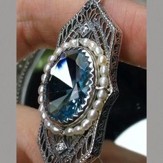 This lovely Antique reproduction pendant is 925 silver. The flawless oval cut simulated man-made blue aquamarine is 18mm long and 14mm wide. The huge oval cut gemstone is surrounded by a string of seed pearls for accent. Two 2mm Cubic Zirconia (CZ) gems grace the top and bottom of the face of the pendant in a final sparkle. The pendant is 2" long and 7/8" wide. The bail opening is 3.5mm x 5mm and will thus fit any chain of 3mm or less. The chain (if chosen) is adjustable between 18-20" long. Exquisite Aquamarine Jewelry Gift, Exquisite Aquamarine Jewelry As Gift, Exquisite Aquamarine Jewelry For Gift, Exquisite Blue Topaz Jewelry In Blue, Exquisite Blue Topaz Jewelry, Elegant Aquamarine Blue Jewelry, Elegant Blue Aquamarine Jewelry, Elegant Silver Aquamarine Jewelry, Classic Blue Topaz Pendant Jewelry