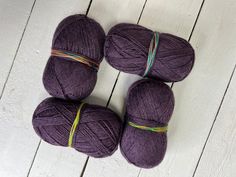 four skeins of purple yarn sitting on top of a white wooden floor