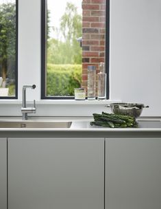 a kitchen sink sitting under a window next to a counter top with vegetables on it