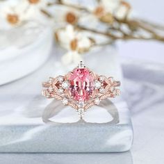 a pink diamond ring sitting on top of a white marble table next to some flowers