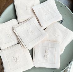 six white embroidered napkins with monogrammed letters on them sitting on a green plate