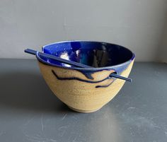 a blue and yellow bowl with chopsticks in it on a gray table next to a white wall