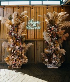 two tall vases with flowers and feathers on the side of a wooden wall next to each other