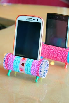 two cell phones sitting next to each other on top of a wooden table in front of a phone holder