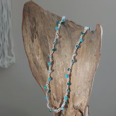 a necklace with blue beads and silver chains on top of a piece of drift wood