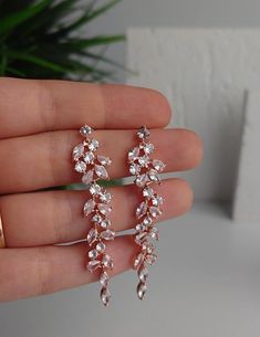 a pair of earrings in the palm of someone's hand with a plant behind them