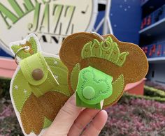 a hand holding a green and brown bear shaped keychain in front of a sign