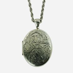 "This vintage sterling silver locket pendant and necklace set was made by highly regarded jeweler, Danecraft.  The large oval locket features engraved decoration on the front consisting of multiple ivy leaves growing along curvilinear stems, all of which are set against a stippled ground.  There is a trio of ivy leaves at the bottom with four c-shaped scrolls positioned around them.  The scrolls have a series of interior rectangular shapes that give them the appearance of stylized thistle blosso Antique Silver Oval Pendant Locket Necklace, Antique Silver Oval Pendant Necklace With Locket, Antique Silver Locket Necklace With Oval Pendant, Antique Silver Necklace With Oval Locket Pendant, Antique Silver Sterling Silver Vintage Locket Necklace, Vintage Sterling Silver Engraved Locket Necklace, Vintage Engraved Sterling Silver Locket Necklace, Vintage Engraved White Gold Necklace, Ornate Engraved Antique Silver Locket Necklace