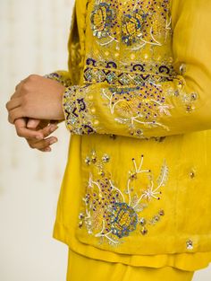 Editor's Note Mustard Hand Embroidered Jacket With Matching Peplum And Sharara In Crepe Fabric: Crepe, Organaza Color: Mustard Care: Dry Clean Only About the Designer Sanya Gulati's designs are inspired by the Indian bridesmaids, pastel easy hues & seasonal trends, her designs are a mix of modern, contemporary embroideries with traditional silhouettes thus creating our signature asymmetric checks embroideries amalgamated with floral thread work, through her designs, the designer aims to enhance Wedding Straight Kurta With Intricate Embroidery, Festive Tops With Floral Embroidery For Eid, Yellow Festive Top For Eid, Festive Floral Embroidery Tops For Eid, Embroidered Long Sleeve Wedding Top, Festive Floral Embroidered Straight Kurta Blouse, Festive Straight Kurta Top With Dabka Work, Festive Dabka Work Straight Kurta Top, Spring Bandhgala With Chikankari Embroidery And Long Sleeves