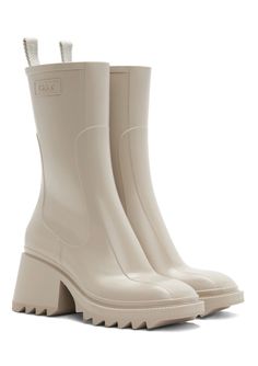 The rubber Betty rain boot reveals a sleek, strong upper recalling classic leather boots and incorporating the Maison's signature contours. The voluntarily oversized back loop shows the Chloé logo, while an internal zipper closure ensures a fitted, feminine silhouette. Short and flat, the square toe shape lends a strong, assertive attitude. The comfortable heel elevates the silhouette, while the bold lugged sole gives an edgy attitude to this rain boot. Chloe Rain Boots, Chloe Betty Boots, Pvc Boots, Chloe Logo, Chloe Clothing, Boots Beige, Wellington Boots, Comfortable Heels, Classic Leather