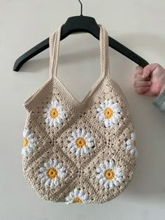 a crocheted bag hanging on a hanger with a hand holding it up