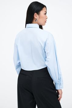 Our Ezra Shirt is a capsule wardrobe dream for your closet. Crafted from 100% crisp European poplin cotton, she offers a classic button-up silhouette in front, but with a cropped back for modern edge. Say hello, as well, to her diagonal seams at the front, sleek collar and long dolman sleeves finished with mother-of-pearl button cuffs. Wear Ezra tucked, tied or open and free—she never fails to inspire new looks.[SPLIT] Shannon, in light blue, is 5'8" (173 cm) tall, wearing a size M. Rocio, in li Formal Button-up Poplin Tops, Formal Poplin Button-up Top, Classic Cropped Shirt With Button Cuffs, Chic Fitted Cropped Shirt With Button Cuffs, Fitted Cropped Shirt With Button Cuffs For Work, Classic Cropped Shirt For Daywear, Chic Poplin Shirt For Work, Classic Cropped Shirt, Classic Fitted Cropped Shirt For Work