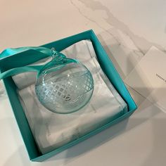 a glass ornament in a blue box on a white tablecloth with a green ribbon