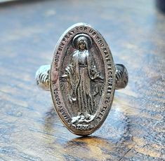 I converted a vintage Miraculous Medal into a pretty & comfortable ring... the traditional Miraculous Medal measures 22x13mm, the ring is a size 5 & 1/2.   I've kept all the beautiful traditional imagery on the back of the Miraculous Medal where it can rest against your skin. This ring is solid sterling silver, stamped Sterling on the inside. I go to estate sales and I love to purchase vintage or antique religious medals whenever I see them - it's fascinating to feel the smooth surfaces & wonder about how often it's been prayed over or blessed...often the top loop has worn away over time, so I like to make these into finger rings so they can be reborn into another life... ~ gift box included! Vintage Hallmarked Rings For Memorial, Vintage Silver Signet Ring With Antique Finish, Vintage Adjustable Open Signet Ring, Vintage Antique Silver Signet Ring For Anniversary, Vintage Nickel-free Antique Silver Rings, Vintage Silver Ring With Antique Finish, Vintage Silver Engraved Oval Ring, Vintage Open Signet Ring, Vintage Handmade Oval Engraved Ring