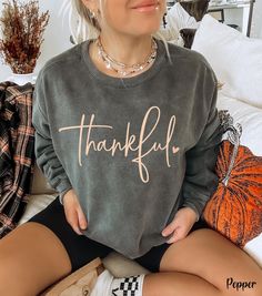 Embrace the cozy vibes of the fall season with our Thankful Sweatshirt, perfect for Thanksgiving and Friendsgiving celebrations! This cute fall sweatshirt features the word "thankful" in a beautiful cursive font, accented with a dainty heart, adding a touch of elegance to your autumn wardrobe. Crafted on a Comfort Colors fall crewneck, this Thanksgiving crewneck sweatshirt is the ideal choice for those chilly days spent at the pumpkin patch or gathering with loved ones. Whether you're dressing u Fall Loungewear Sweatshirt, Comfy Cozy Fit Fall Tops, Comfy Cozy Fit Tops For Fall, Fall Sweater With Letter Print And Long Sleeves, Comfy Fall Tops, Comfy Cotton Sweater For Fall, Long Sleeve Sweater With Letter Print For Fall, Comfortable Crew Neck Fall Sweater, Comfortable Crew Neck Sweater For Fall