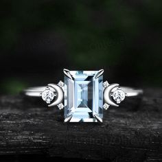 an aqua blue topazte and diamond ring on a piece of wood with green leaves in the background