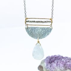 Embrace the enchanting allure of our Moonstone Radiance Necklace, a harmonious blend of celestial elegance and artistic craftsmanship. At its heart, a large moonstone, glowing with an ethereal light, gracefully hangs from a textured silver half circle, capturing the essence of lunar mystique. Above, a delicate gold rectangle, meticulously adorned with tiny sparkling pyrite gemstones, stretches the length of the disc, adding a touch of subtle brilliance to the design. The interplay of textures an Silver Teardrop Celestial Jewelry, White Moon Shaped Mystical Necklace, Mystical Moon Shaped White Necklace, Mystical White Moon-shaped Necklace, Mystical White Moon Necklace, Unique Moon-shaped Moonstone Necklace, White Half Moon Celestial Jewelry, Silver Crescent Moonstone Necklace, Ethereal Silver Moonstone Jewelry