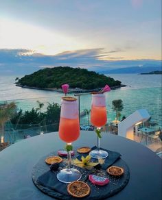 two drinks are sitting on a table overlooking the water and an island in the distance