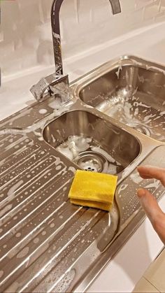 a person cleaning a kitchen sink with a yellow towel on the edge and two soapy dishes next to it