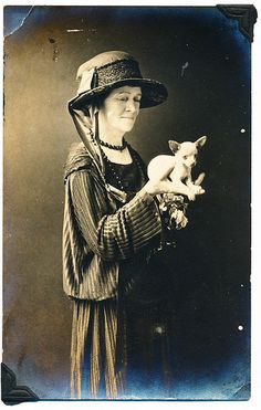 an old photo of a woman holding a small dog and wearing a hat on her head