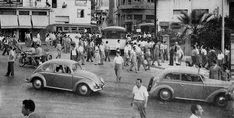 an old black and white photo of people crossing the street in front of some cars