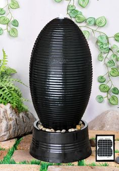 a large black vase sitting on top of a wooden table next to rocks and plants