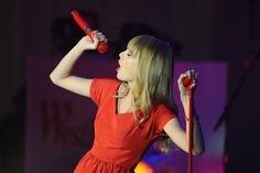 a woman in a red dress is holding a microphone and looking up at the sky