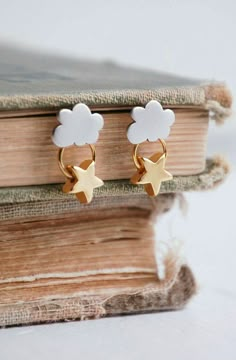 a pair of gold and white earrings sitting on top of a book with clouds in the background