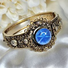 Stunning Art Deco filigree hinged bracelet circa 1930's. Beautiful gold tone lacy filigree metal work and a large blue glass Cabochon. Clasp fastens snugly. Inside measurement is approximately 7¼ inches. There is some wear to the gold plating consistent with age. Please refer to the photos. In overall wonderful vintage condition. Luxury Ornate Cabochon Bracelets, Vintage Cabochon Jewelry For Vintage Collection, Victorian Brass Cabochon Jewelry, Ornate Metal Bangle Jewelry, Victorian Metal Jewelry With Antique Finish, Vintage Blue Cabochon Jewelry, Blue Vintage Cabochon Jewelry, Gold Cabochon Bangle Jewelry, Victorian Style Antique Finish Metal Jewelry